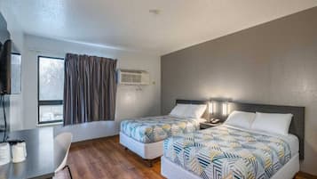 A hotel room with two beds, a desk, a chair, and a window with curtains.