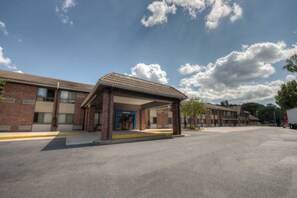 Un bâtiment doté d’une entrée abritée, d’un parking et surplombant un ciel dégagé parsemé de nuages.