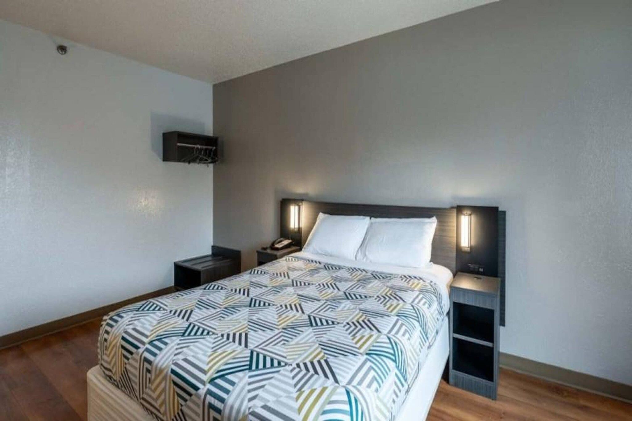 A bedroom with a bed, bedside tables, a wall-mounted TV, and a patterned bedspread.