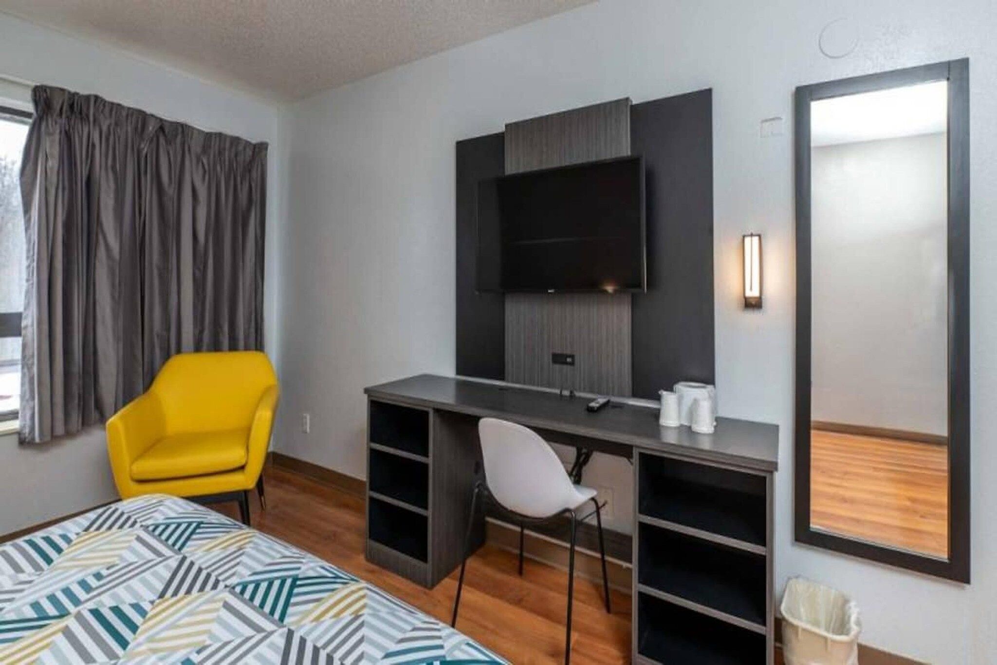 Une chambre d’hôtel avec un lit, un bureau, une chaise, une télévision et une fenêtre avec des rideaux.