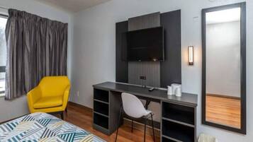 A hotel room with a bed, a desk, a chair, a TV, and a window with curtains.