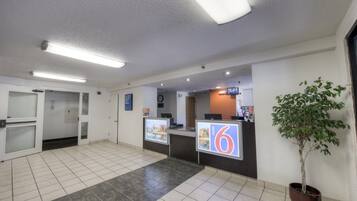 A hotel reception area with a reception desk, a clock, and a potted plant.