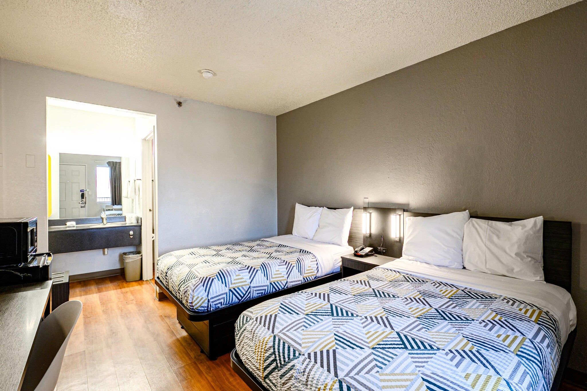 A hotel room with two beds, a desk, and a bathroom visible through an open door.