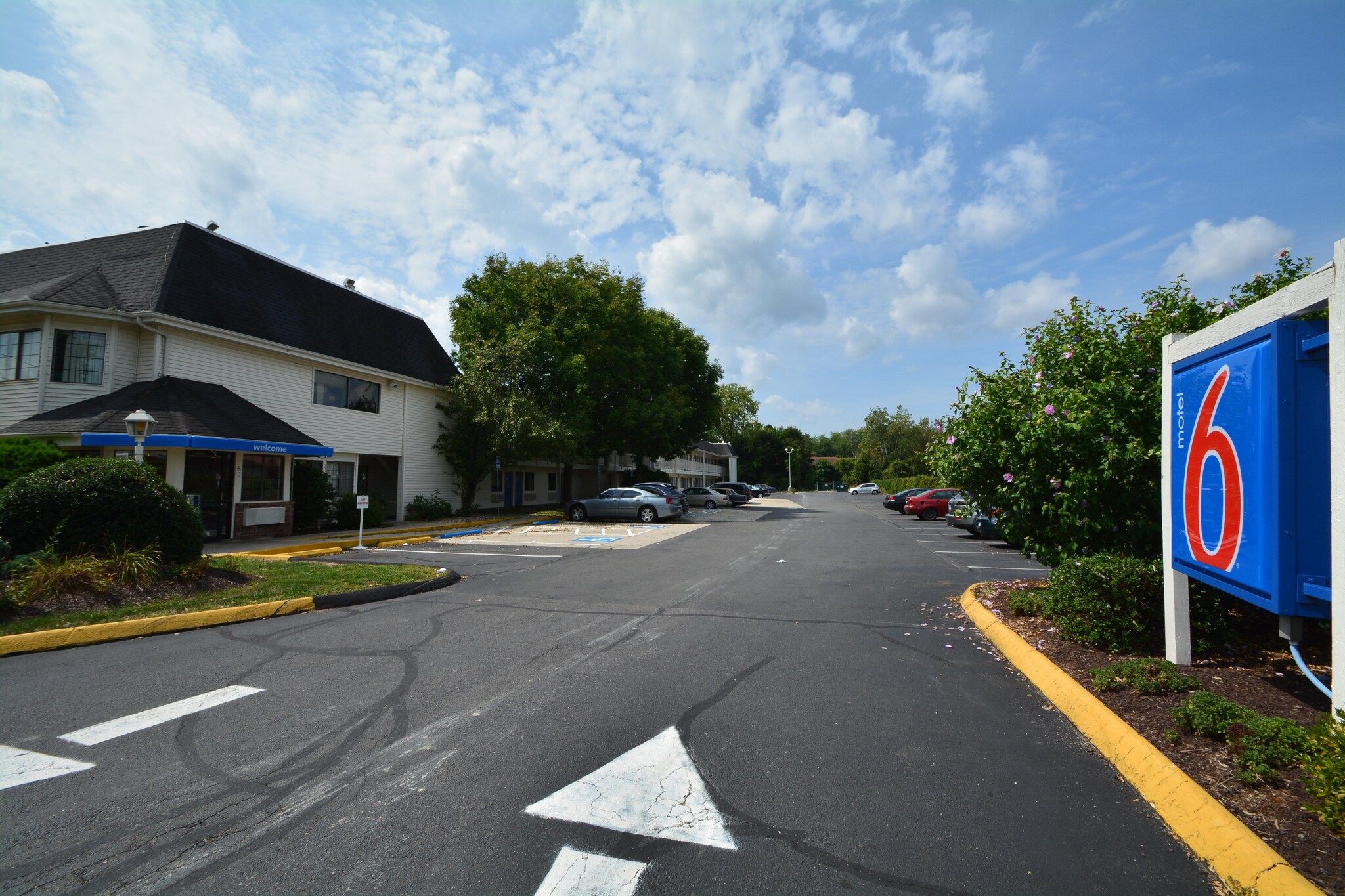 Un motel avec une enseigne bleue, un parking et un bâtiment sur lequel on peut lire « Bienvenue ».