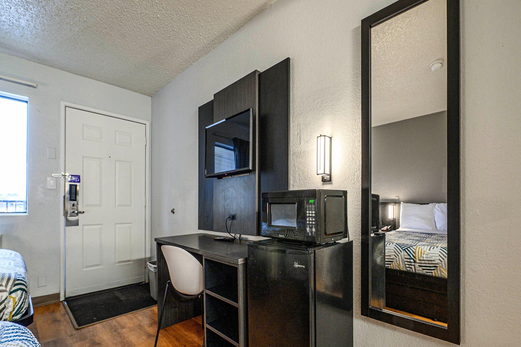 A compact hotel room with a desk, a microwave, a TV, and a bed with a patterned bedspread.