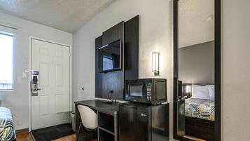 A compact hotel room with a desk, a microwave, a TV, and a bed with a patterned bedspread.