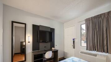 Une chambre d’hôtel avec un lit, un bureau, une chaise, une télévision, une porte et une fenêtre avec des rideaux.
