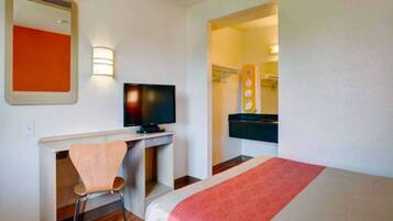 Una habitación de hotel con cama, escritorio con silla, televisor y espejo.