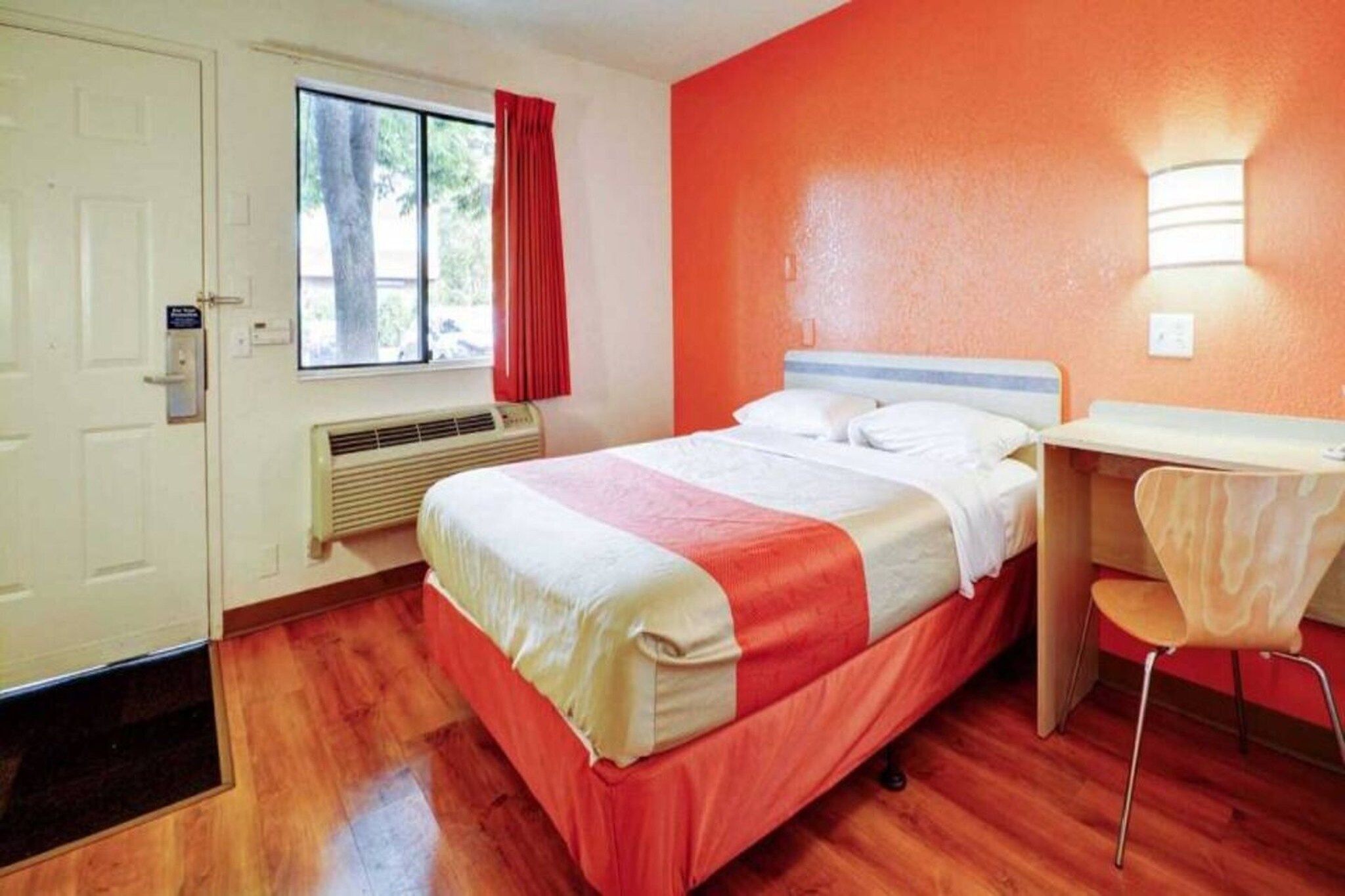 Een hotelkamer met een bed, een bureau, een stoel, een raam met gordijnen en een deur.