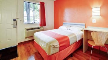 Een hotelkamer met een bed, een bureau, een stoel, een raam met gordijnen en een deur.