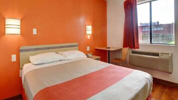 Een hotelkamer met een bed, nachtkastje, stoel, raam en een airconditioning.