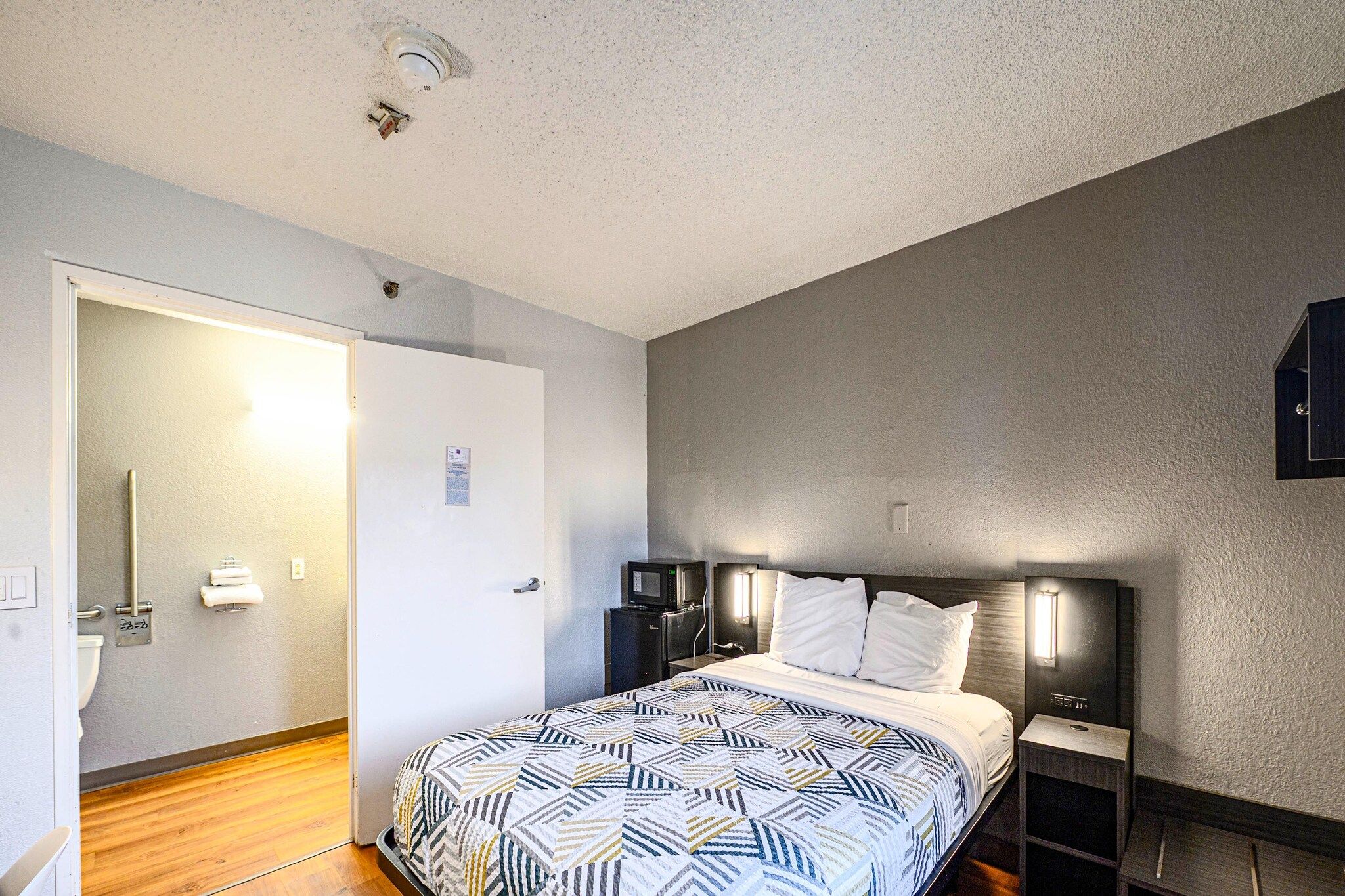 Een hotelkamer met een bed, nachtkastjes, een magnetron en een deur naar een badkamer.