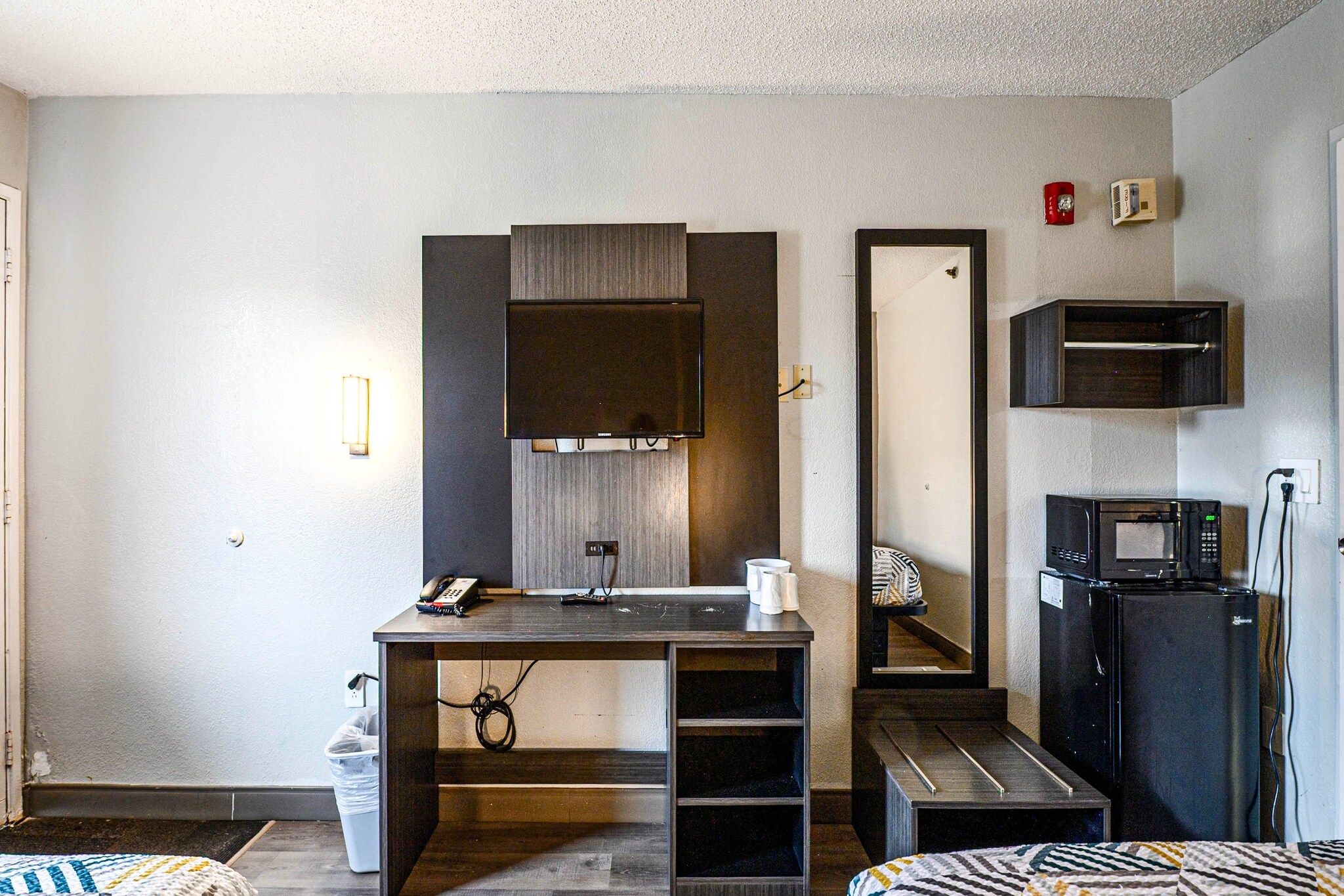 Een compacte hotelkamer met kitchenette, bureau met telefoon, spiegel en magnetron.