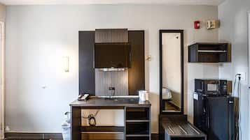 Een compacte hotelkamer met kitchenette, bureau met telefoon, spiegel en magnetron.