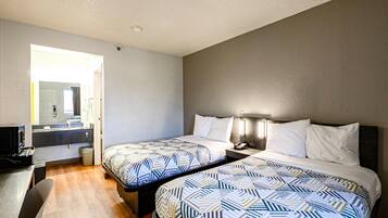 A hotel room with two beds, a desk, and a bathroom visible through an open door.