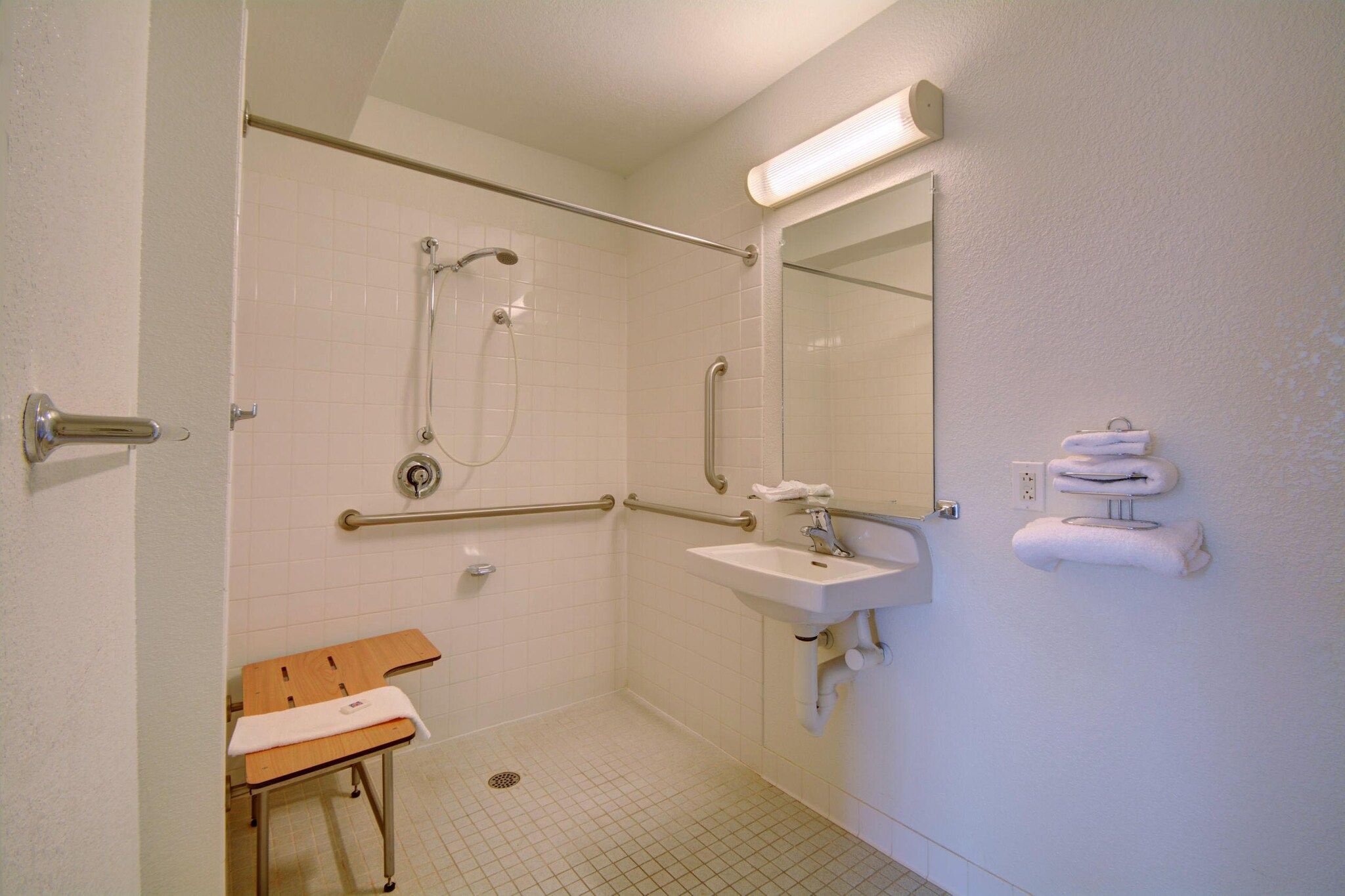 Een toilet dat toegankelijk is voor rolstoelen, met een douche, wastafel en een zitje.