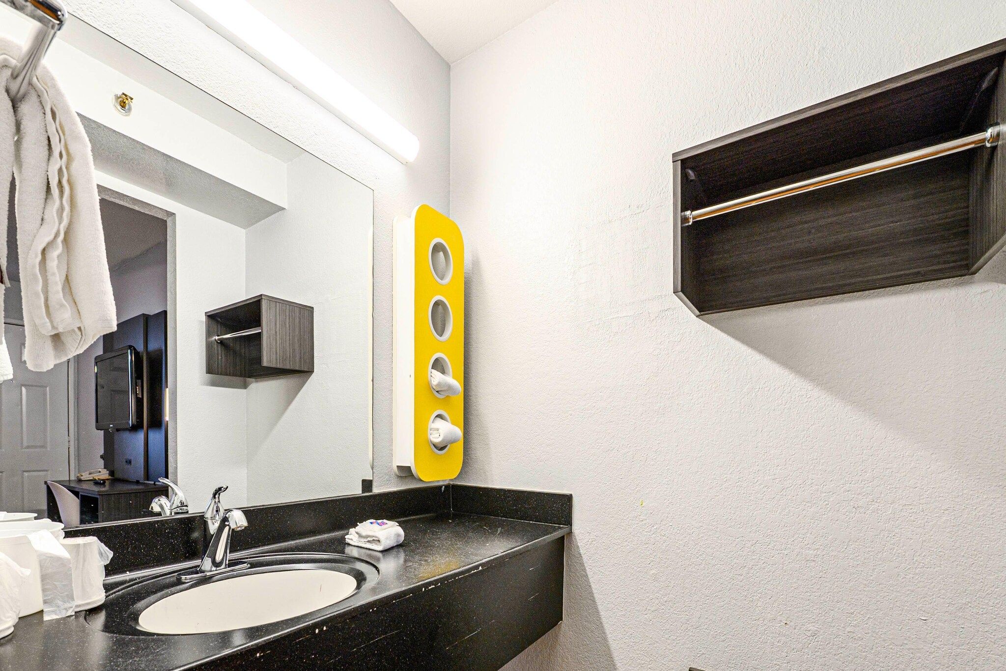 Ein modernes Badezimmer mit einem schwarzen Waschbecken, einem Spiegel, einem Handtuchhalter und einem gelben Seifenspender.
