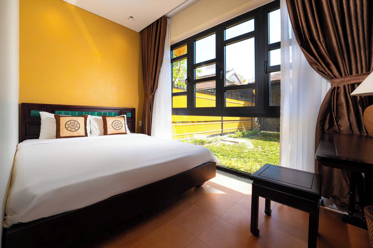A hotel room with a bed, a window with curtains, and a view of a building outside.