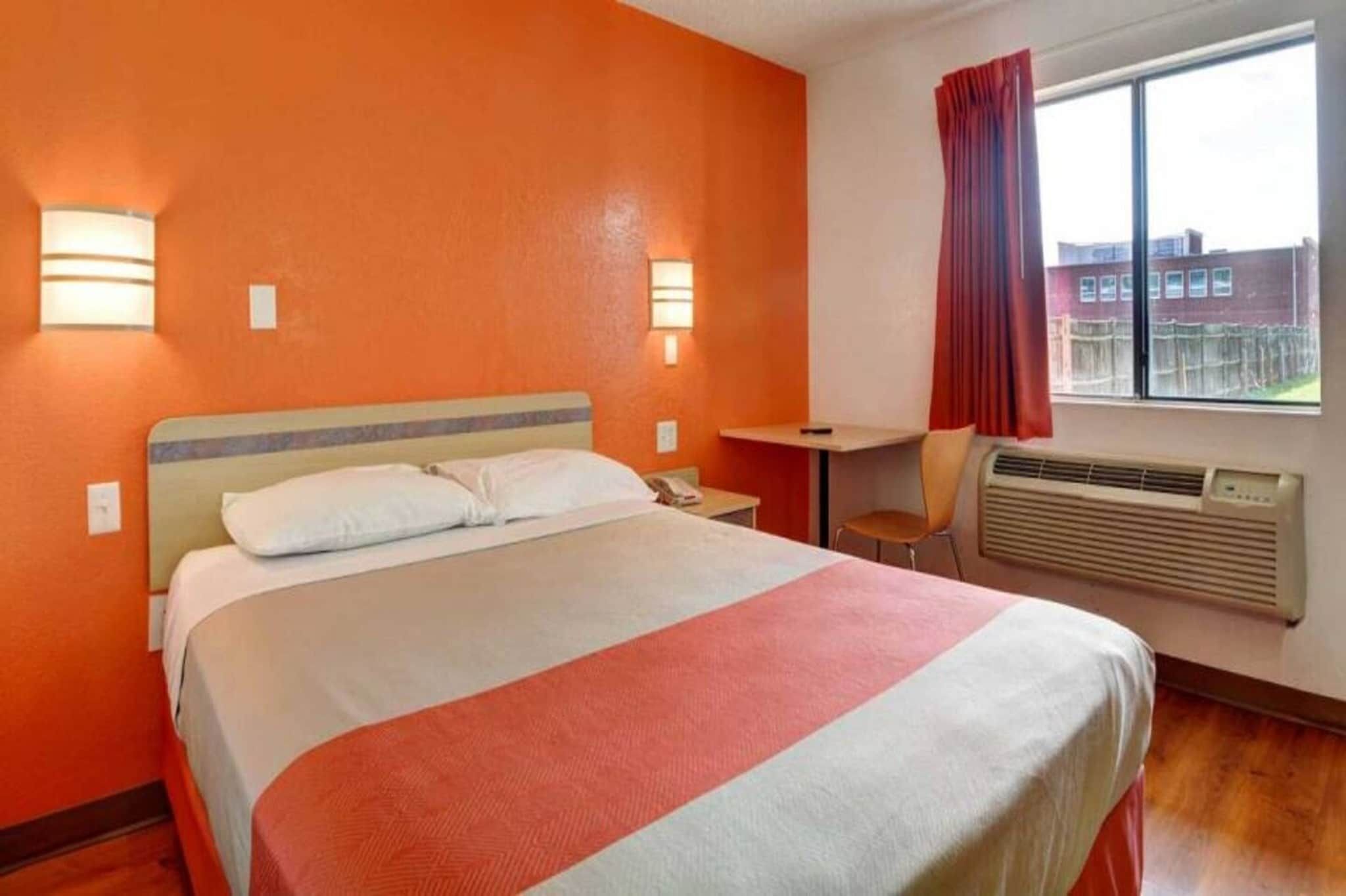 Een hotelkamer met een bed, een bureau, een stoel, een raam met gordijnen en een wandradiator.