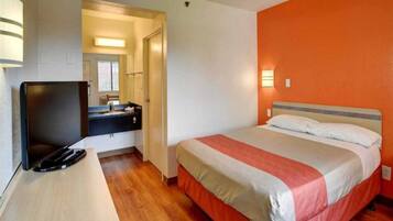 A hotel room with a bed, a desk with a television, a mirror, and a bathroom visible through an open door.