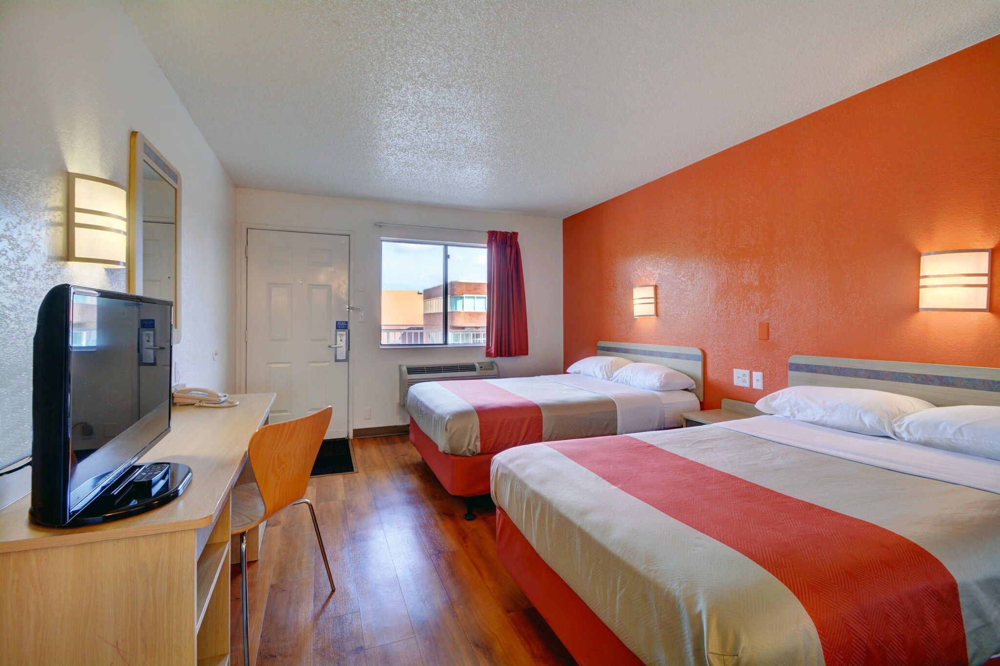 Habitación de hotel con dos camas, un escritorio con televisor y una ventana con cortinas.