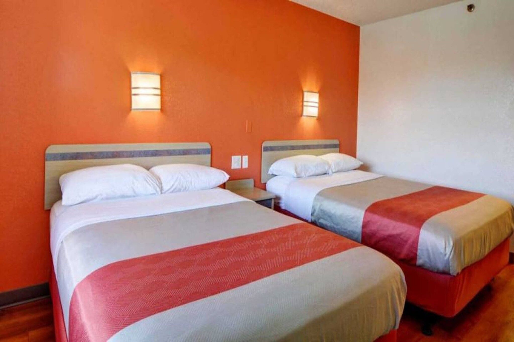 Une chambre d’hôtel avec deux lits, chacun doté d’une tête de lit, et un luminaire fixé au mur.