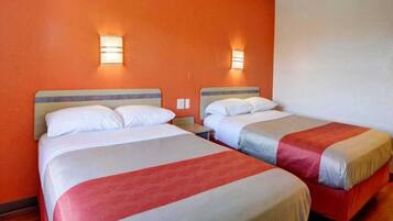 Une chambre d’hôtel avec deux lits, chacun doté d’une tête de lit, et un luminaire fixé au mur.
