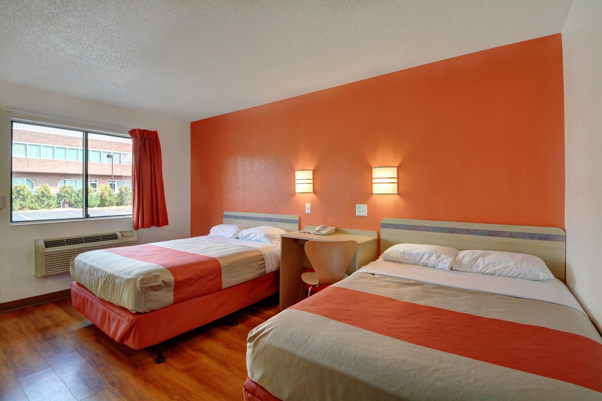 Una camera d'albergo con due letti, una finestra con tende, un comodino e una lampada fissata al muro.