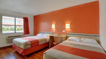 Una camera d'albergo con due letti, una finestra con tende, un comodino e una lampada fissata al muro.