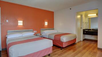 Habitación de hotel con dos camas, piso de madera y baño con espejo y lavamanos.