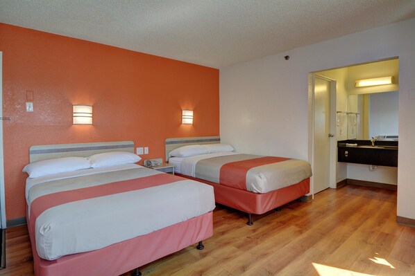A hotel room with two beds, a wooden floor, and a bathroom with a mirror and sink.