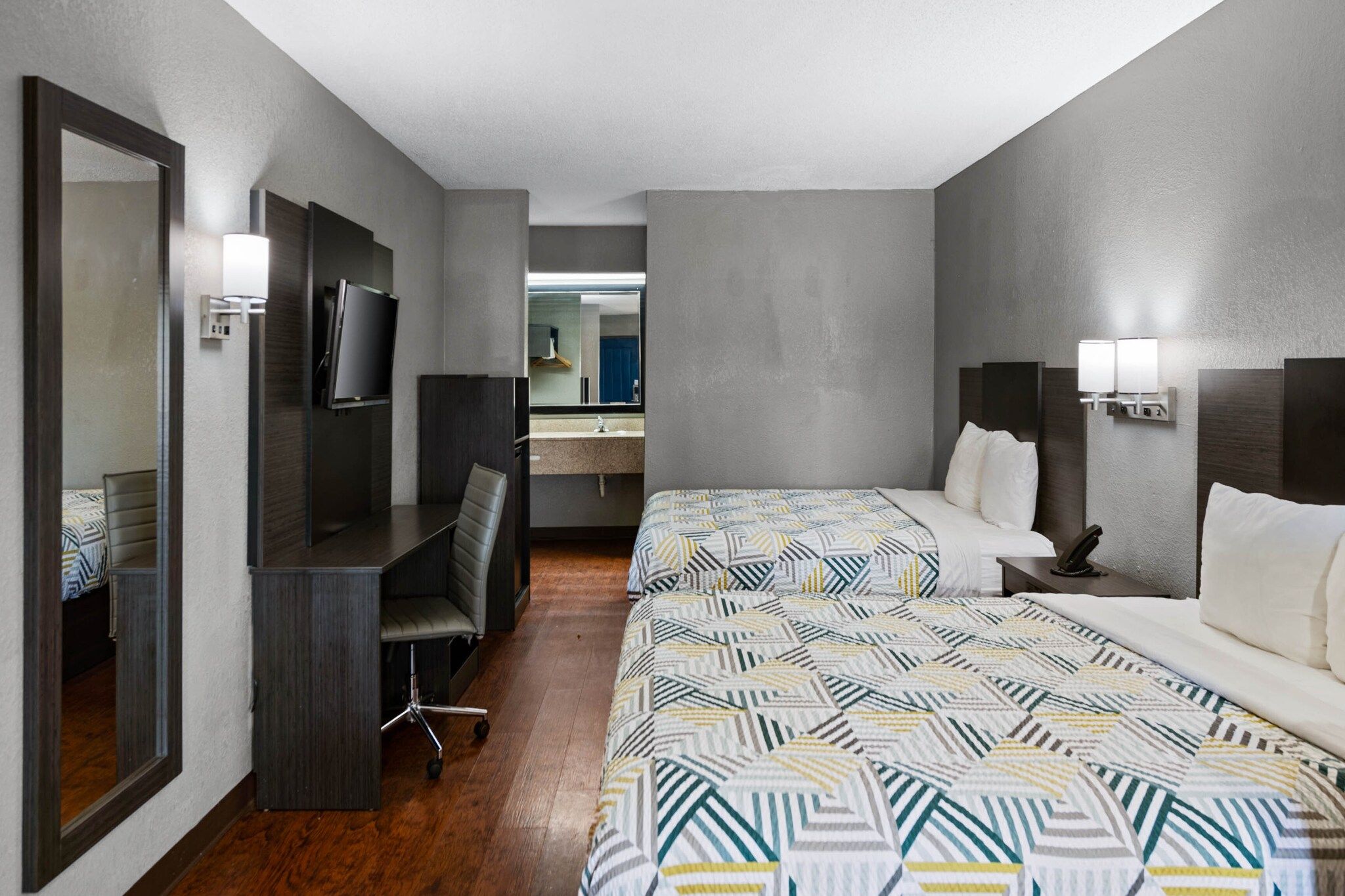 A hotel room with two beds, a desk, a chair, a TV, and a bathroom visible through an open door.
