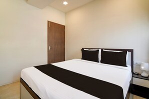 Una habitación de hotel con una cama, una mesita de noche, una lámpara y una puerta.
