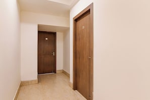 A corridor with two wooden doors, one with a visible number plate, and a tiled floor.