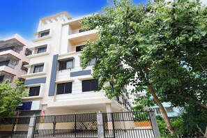 Un edificio residencial de varios pisos con balcones, una entrada con reja y un árbol en primer plano.