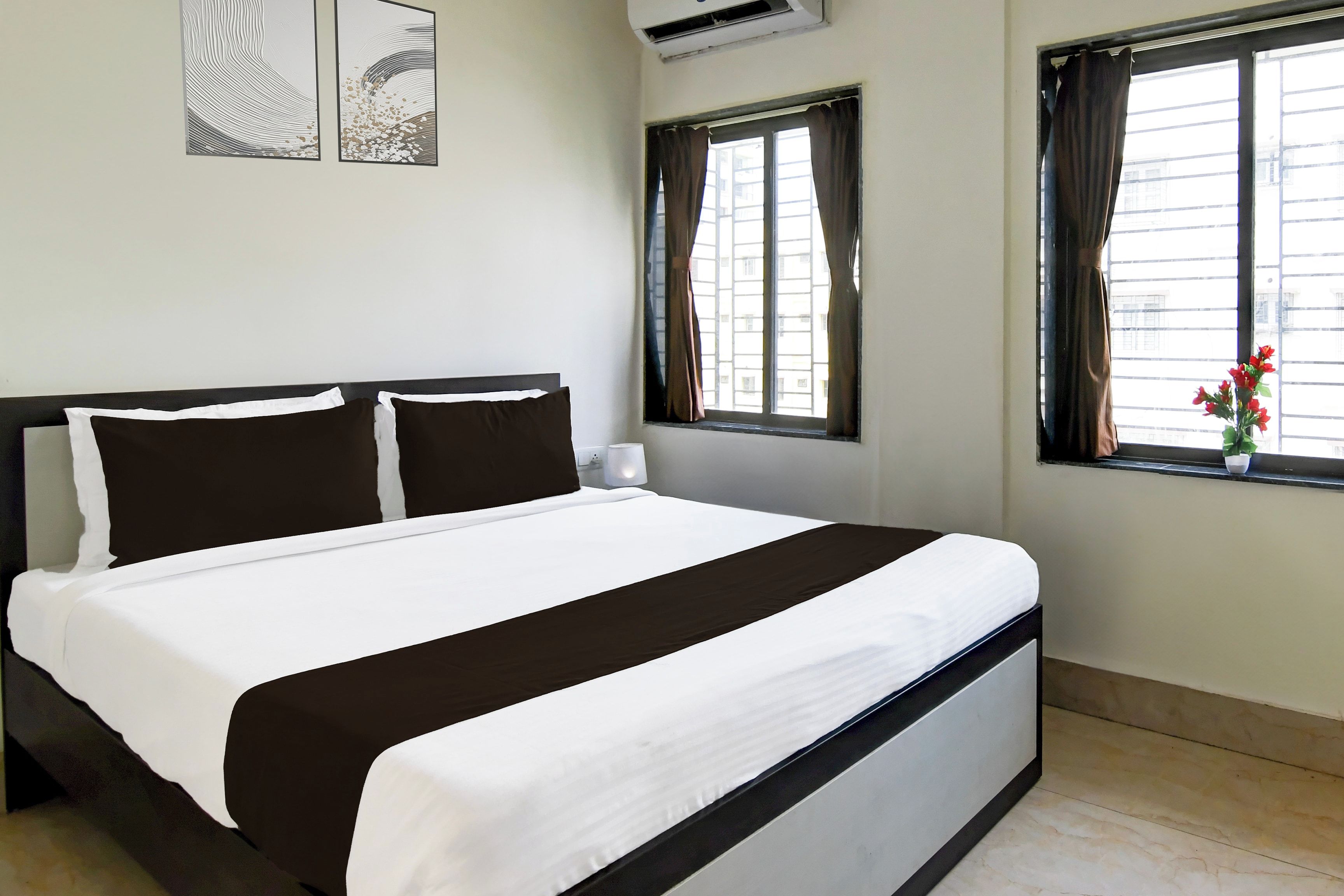 A hotel room with a bed, two wall-mounted air conditioning units, and a window with curtains.