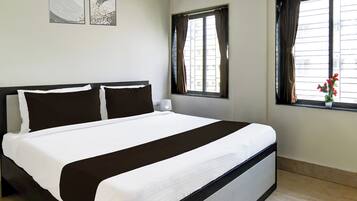 A hotel room with a bed, two wall-mounted air conditioning units, and a window with curtains.