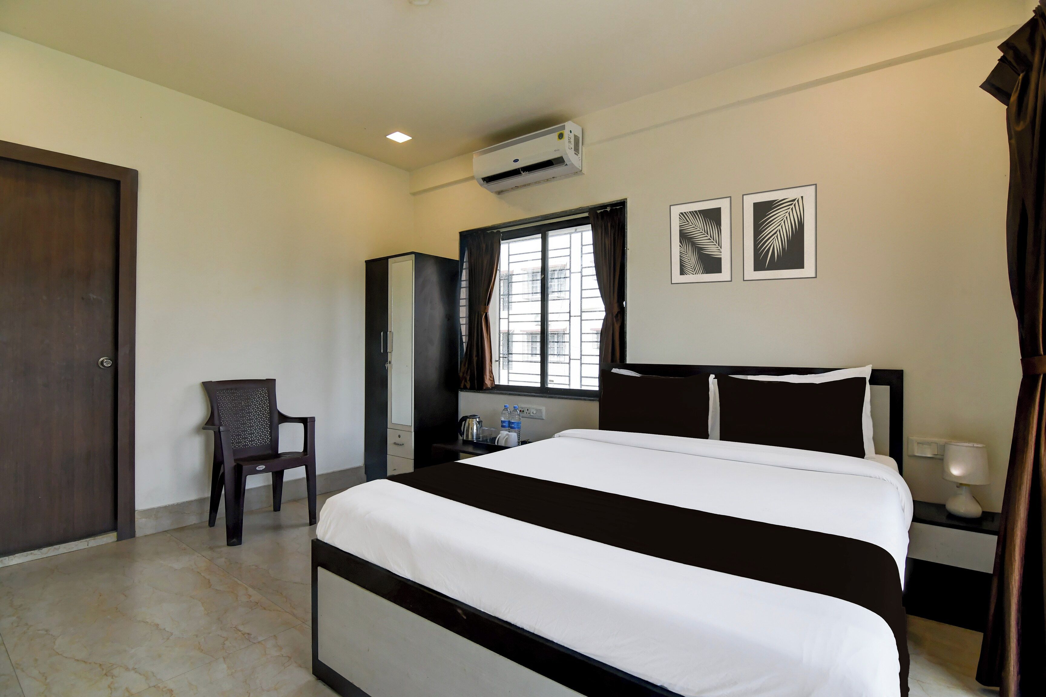 Une chambre d’hôtel avec un lit, un bureau, une chaise, une armoire et une fenêtre avec des rideaux.