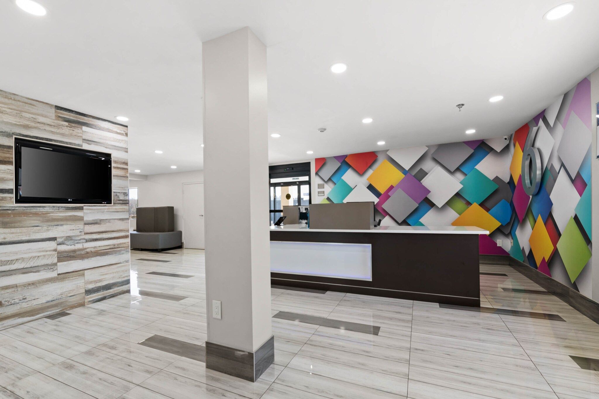 Un área de recepción moderna con un televisor de pantalla plana, una mesa de recepción y un llamativo diseño mural geométrico.