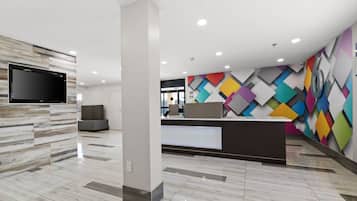 Un área de recepción moderna con un televisor de pantalla plana, una mesa de recepción y un llamativo diseño mural geométrico.