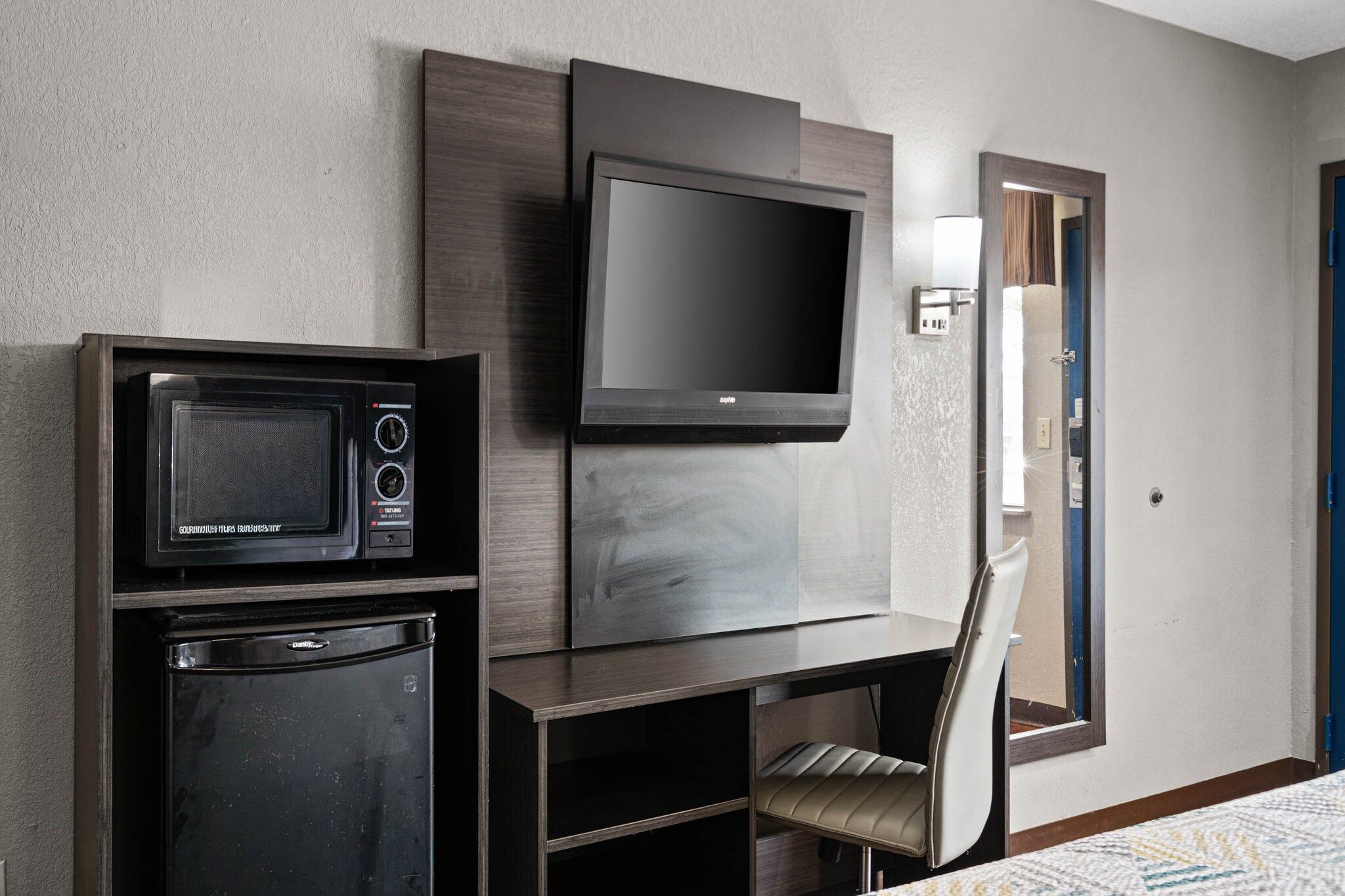 Ein Hotelzimmer mit Flachbildfernseher an der Wand, einer Minikühlschrank, einer Mikrowelle und einem Sessel.