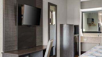A hotel room with a flat-screen TV mounted on the wall, a mirror, a bed with a patterned bedspread, and a bathroom with a sink and mirror.