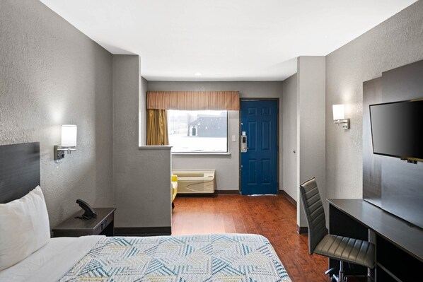 A hotel room with a bed, a desk, a chair, a television, a window with curtains, and a door.
