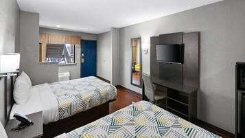 Ein Hotelzimmer mit zwei Betten, einem Fernseher, einem Schreibtisch mit Telefon und einem fensterbepflanzten Fenster.