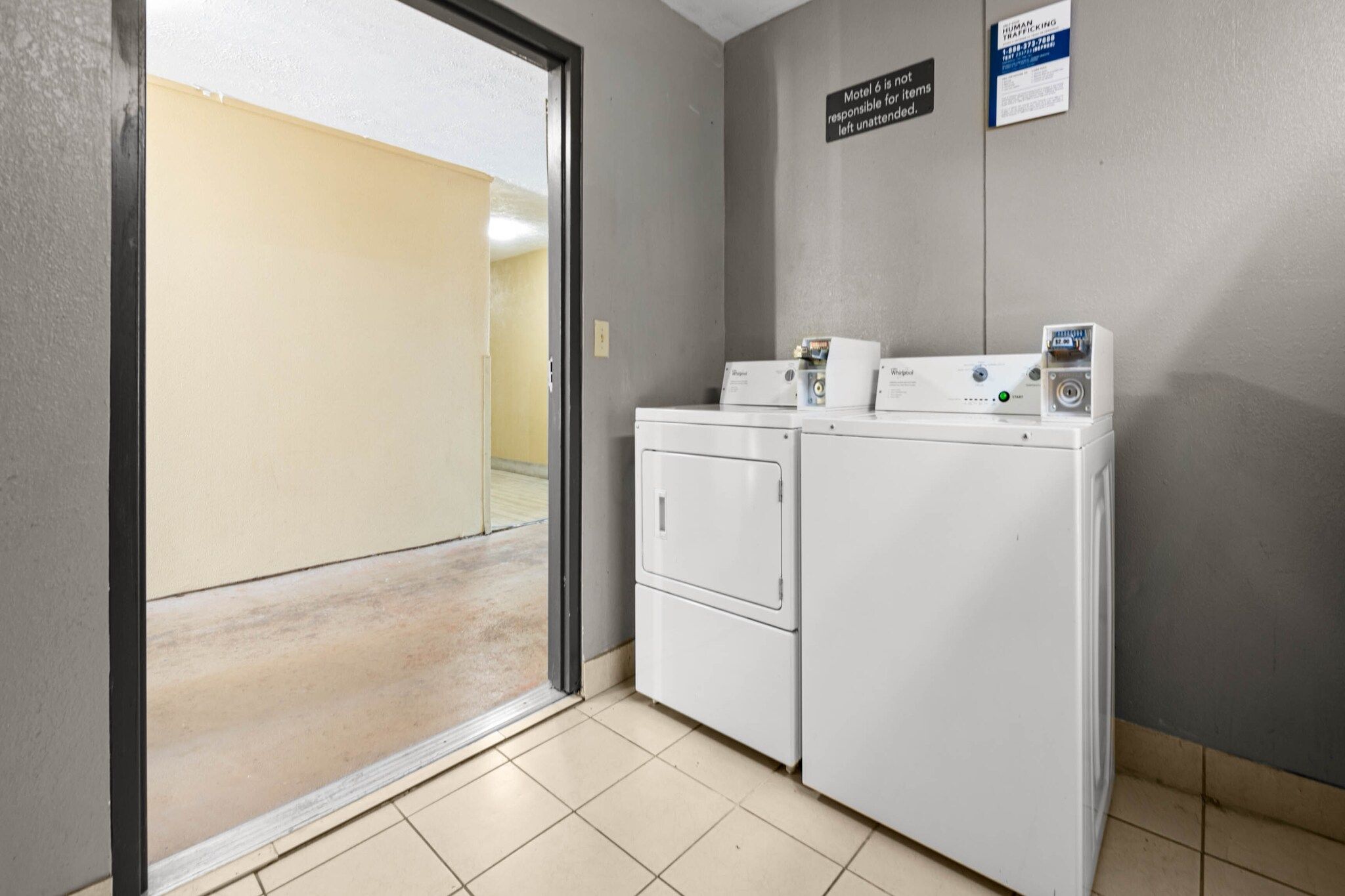 Une buanderie équipée d’un lave-linge et d’un sèche-linge, un panneau indiquant que le motel n’est pas responsable des objets laissés sans surveillance, et une affiche d’information sur la traite des êtres humains.