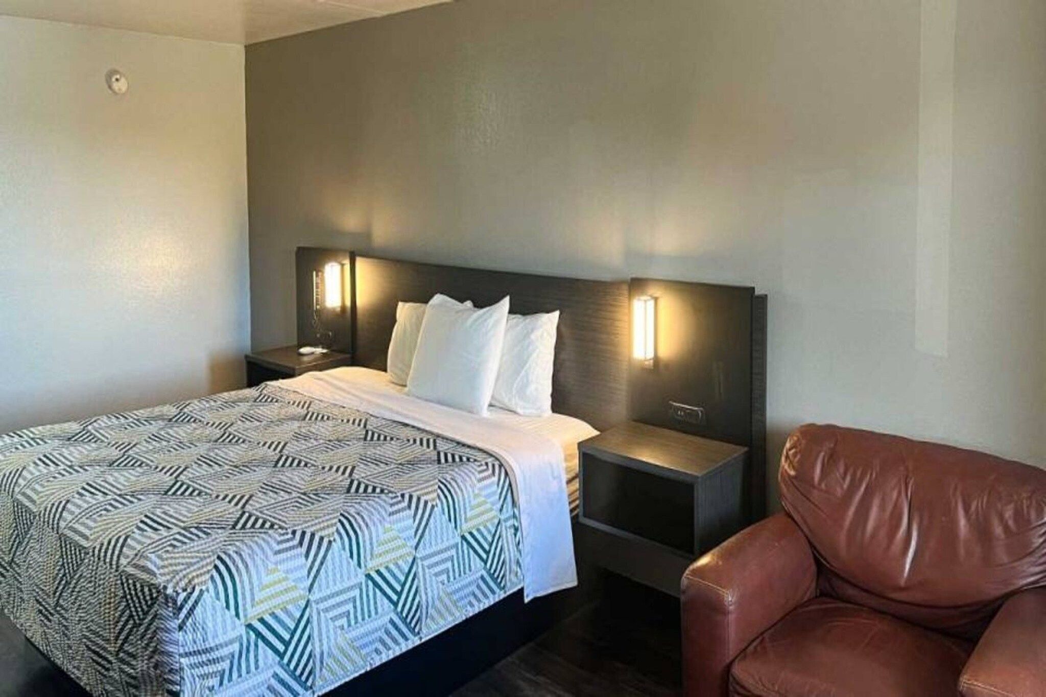 Ein Hotelzimmer mit einem Bett, zwei Nachttischen, einem Sessel und einer Wandleuchte.
