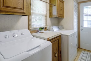 A laundry area with a front-loading washer, a dryer, wooden cabinets, and a window with blinds.
