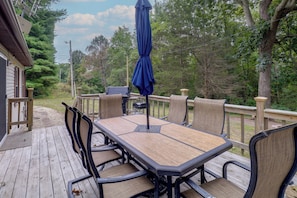 A deck with a table and chairs, surrounded by a wooden railing, overlooking a wooded area.