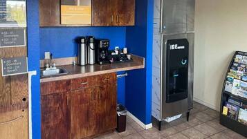 Een kitchenette met een koffiezetapparaat, waterkoker en spoelbak, een roestvrijstalen koelkast en een prullenbak.
