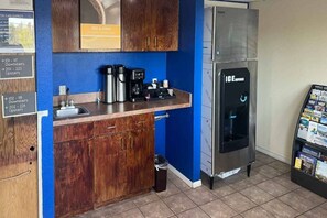 Una kitchenette equipada con cafetera, hervidor de agua y pileta, un refrigerador de acero inoxidable y un basurero.